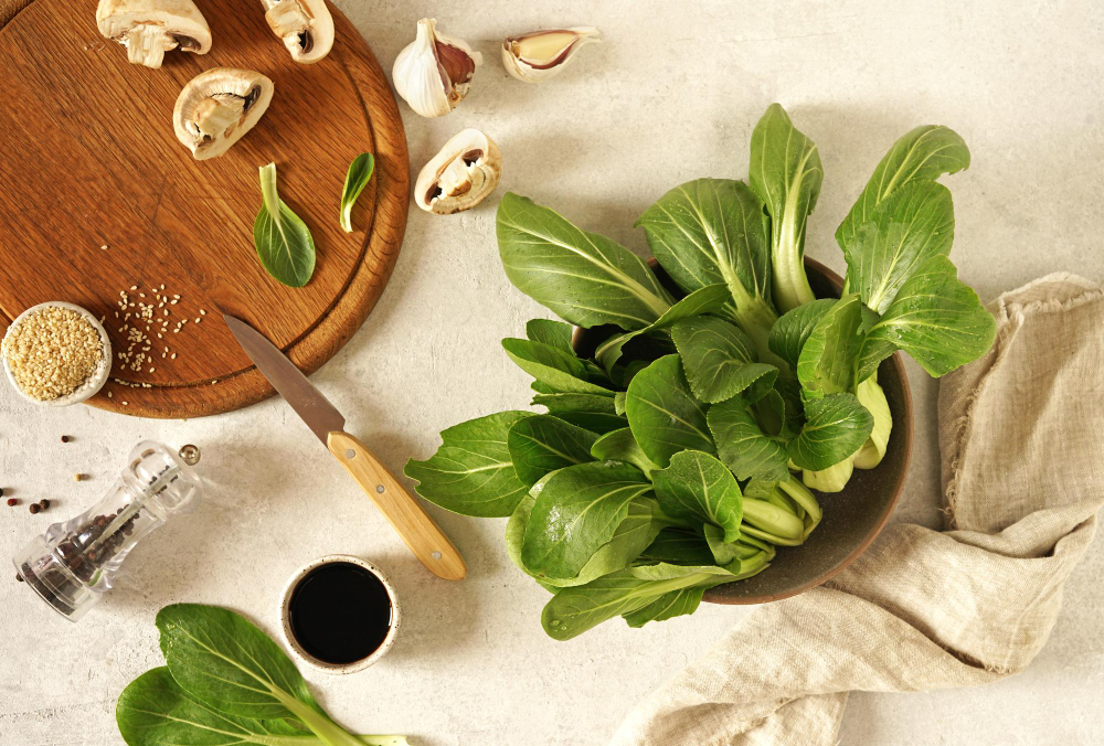 fresh-green-pok-choy-bowl-gray-table-mushrooms-cutting-board-top-view (1)