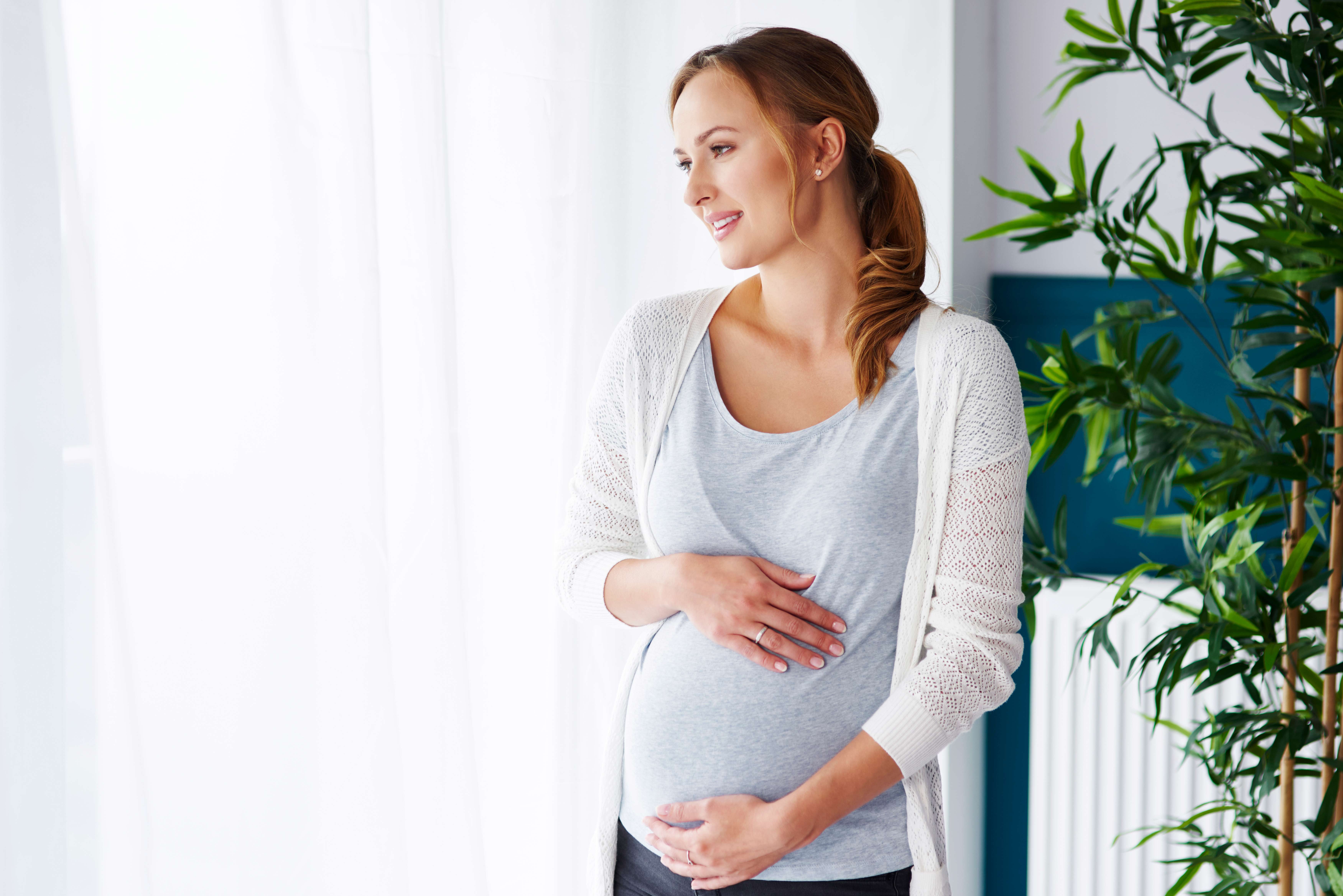 cheerful-pregnant-woman-looking-through-window