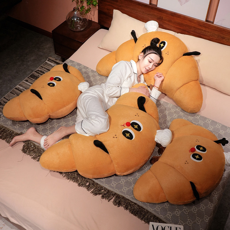 Croissant plush pillow used as a soft bed backrest and lounging cushion, cozy croissant-shaped pillow for relaxing on the bed