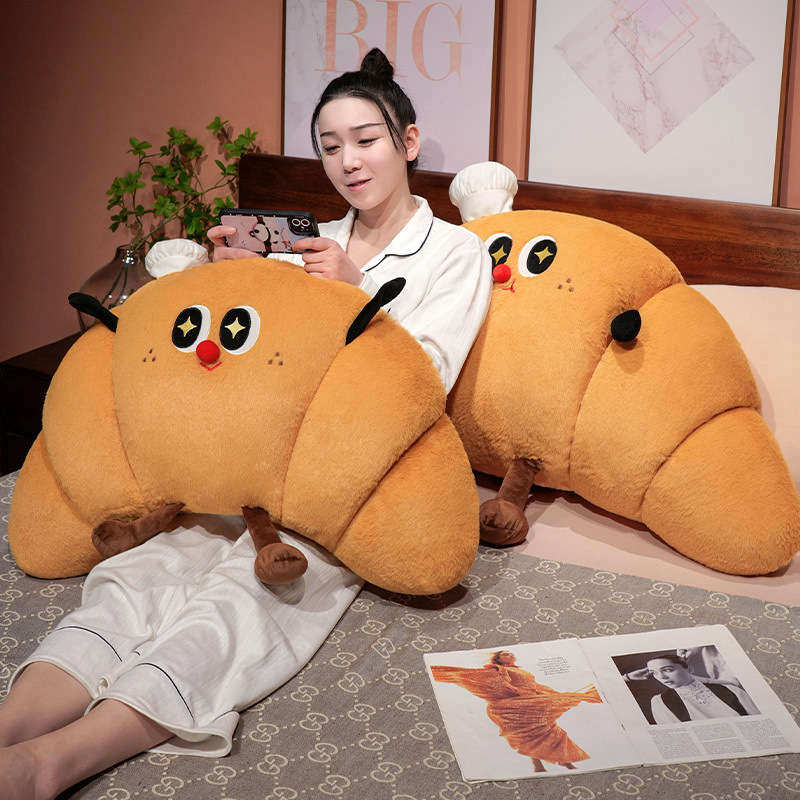 Croissant plush pillow used as a cozy bed backrest cushion, soft croissant-shaped pillow for relaxing, reading, or watching videos in bed