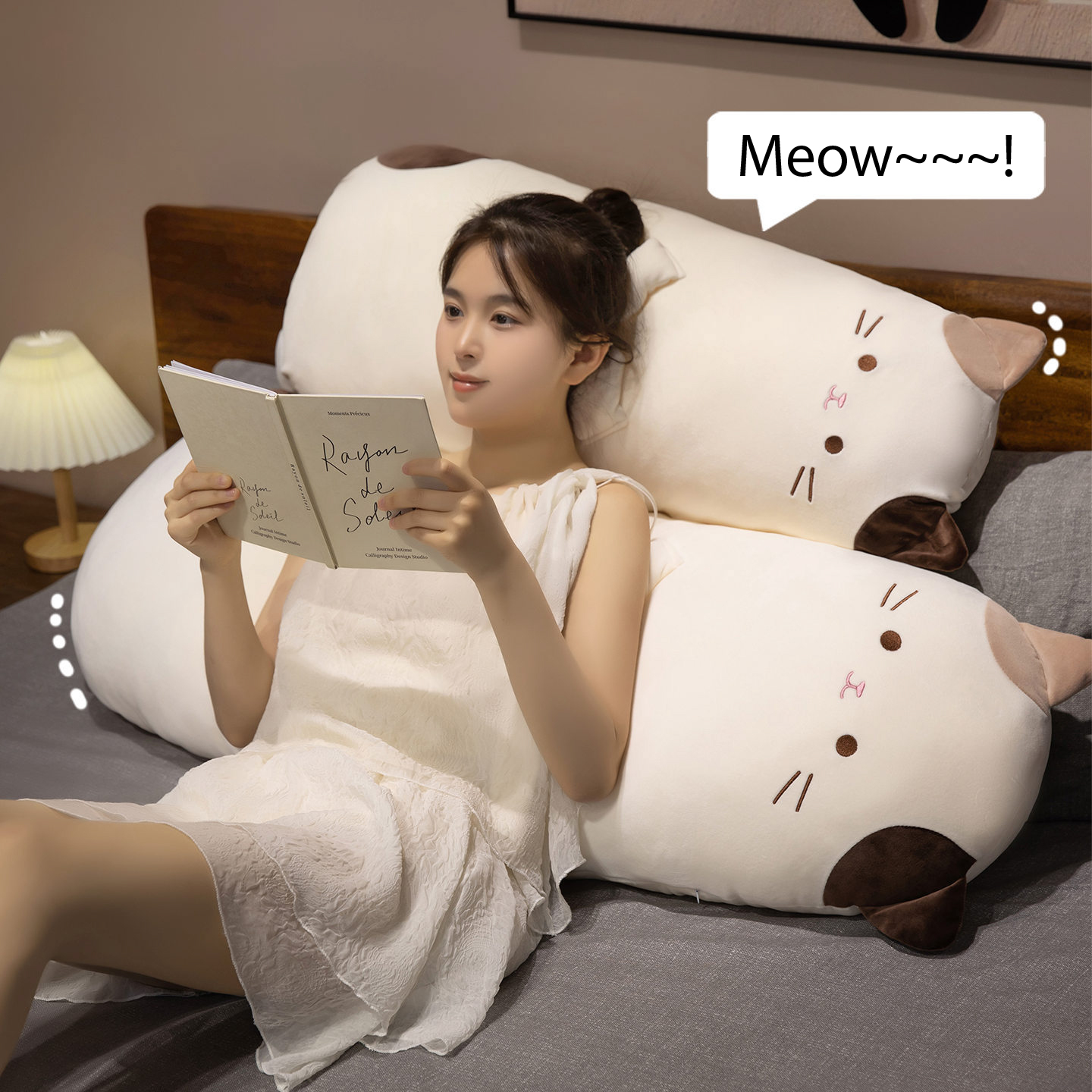 Calico cat long plush pillow used as a soft backrest on a bed, cute plush body pillow perfect for relaxing, reading, or decorating a cozy bedroom