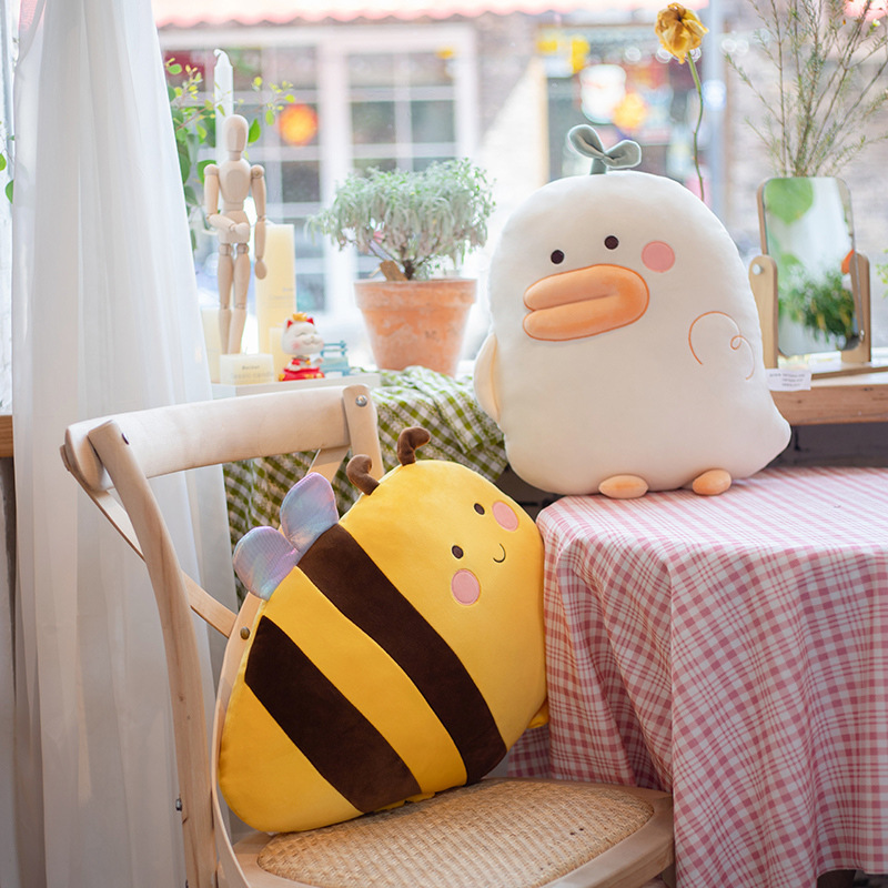 Cute duck and bee plush pillows placed by the window and chair, soft hugging cushions for cozy home decoration