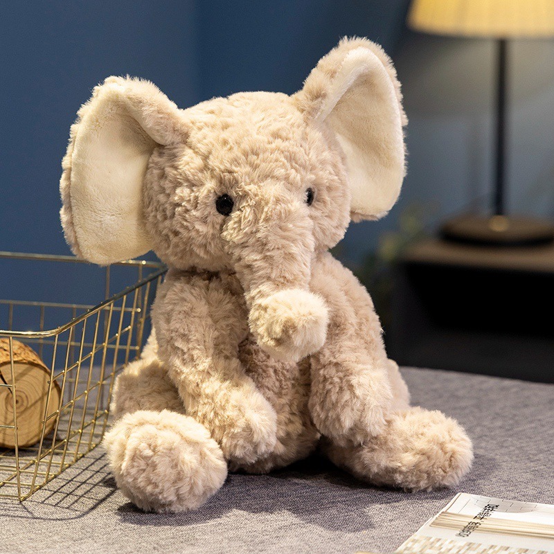 Cute elephant plush toy with soft fluffy texture in a sitting pose, displayed on a tabletop with warm ambient lighting for cozy home decor