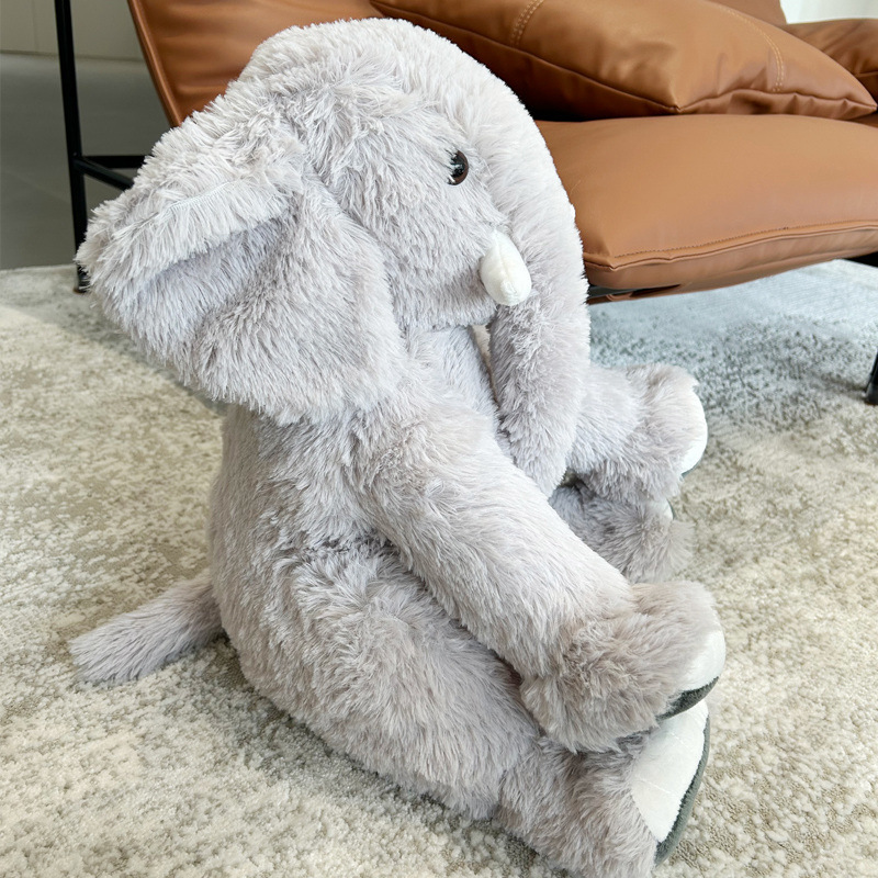 Gray elephant plush toy sitting on a carpet beside a sofa, soft fluffy texture and cozy home setting
