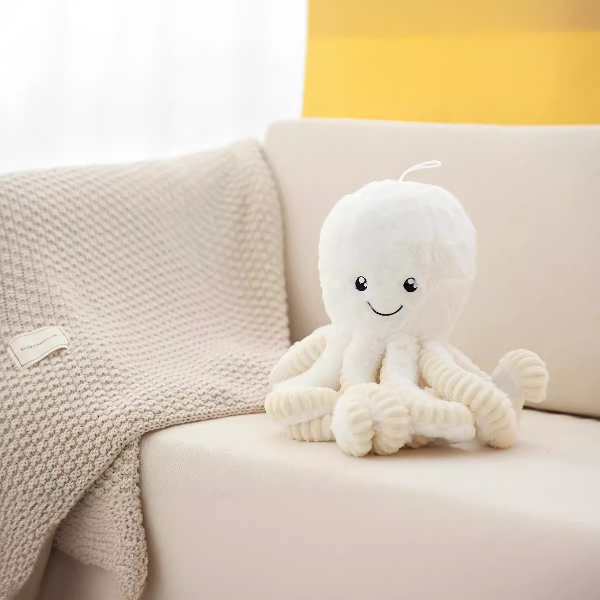 White octopus plush toy sitting on a sofa with soft knit blanket, creating a calm and cozy home decor atmosphere