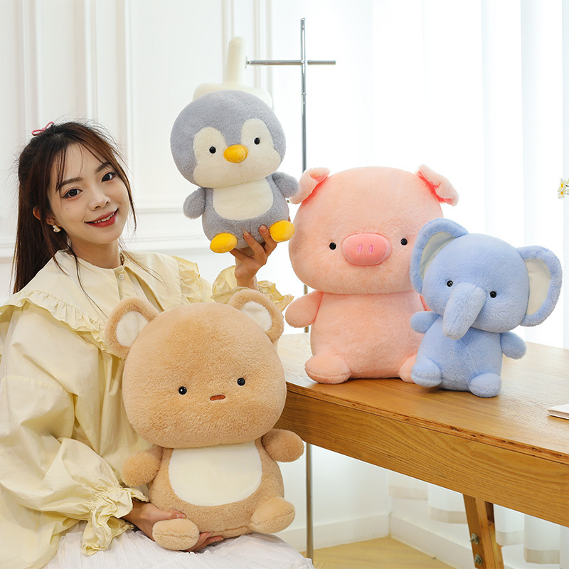 Soft animal plush toys including pig, elephant, bear, and penguin displayed together on a table, showcasing smooth plush texture and adorable rounded shapes in a cozy home setting
