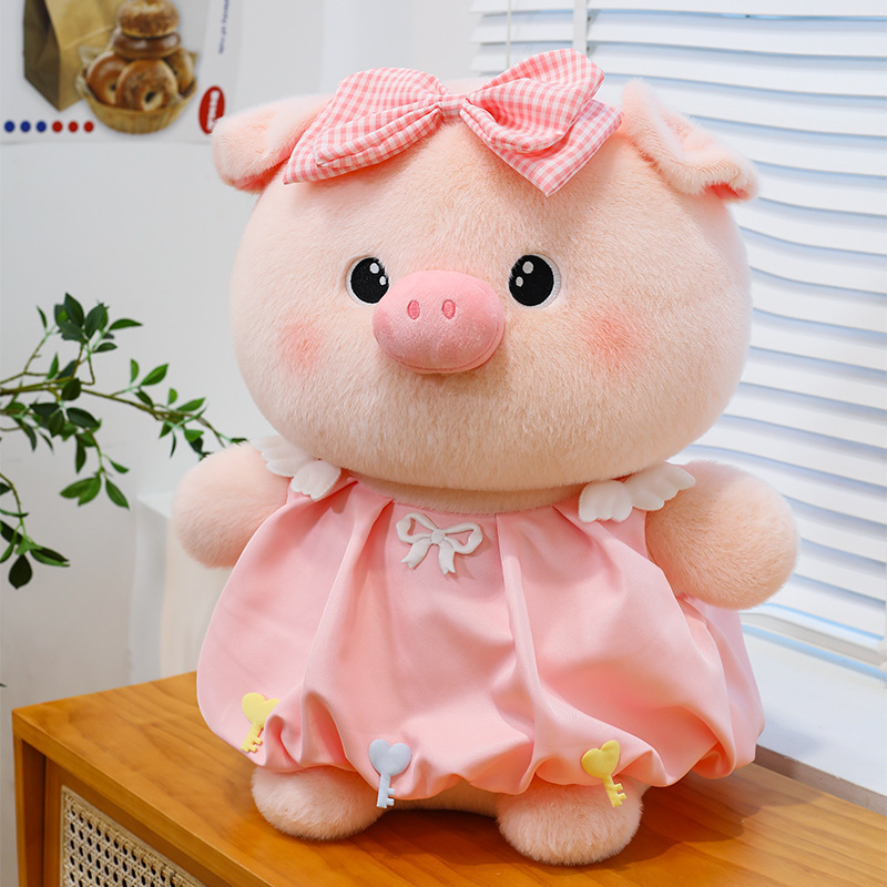 Bubble pig plush toy in pink dress with bow detail placed on wooden surface, soft plush fabric and rounded design, suitable for display and cozy room decor