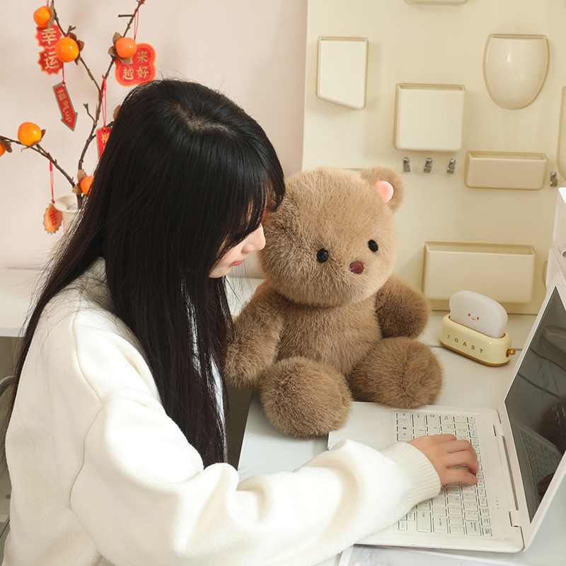 Bear plush toy placed beside a laptop on a desk, soft fluffy texture in a cozy workspace setting, adding comfort and warmth to daily routines