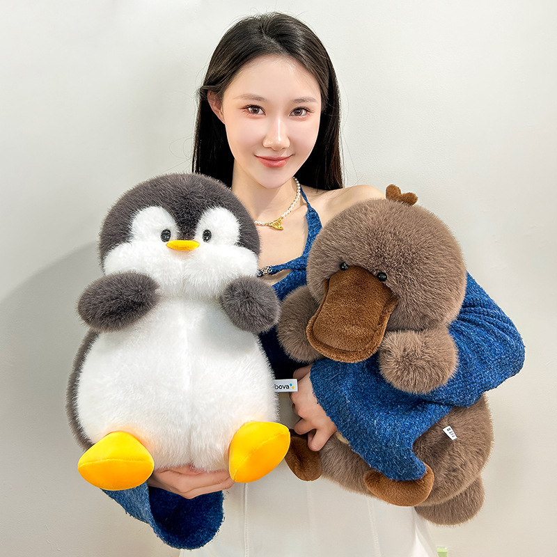 Penguin and platypus plush toys held in arms, soft cuddly stuffed animals with fluffy texture for hugging and comfort