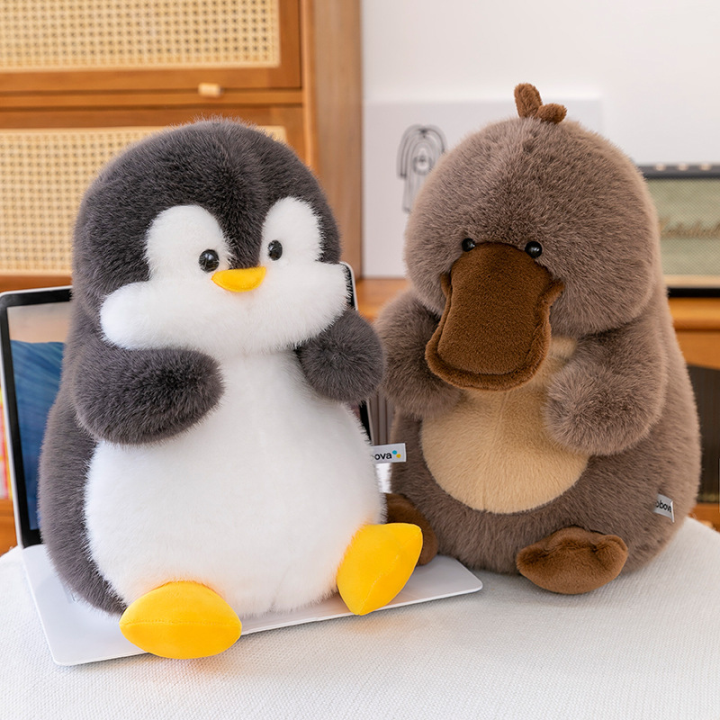 Penguin and platypus plush toys sitting on a desk, soft fluffy texture, cute animal design, cozy decorative stuffed toys for home or workspace