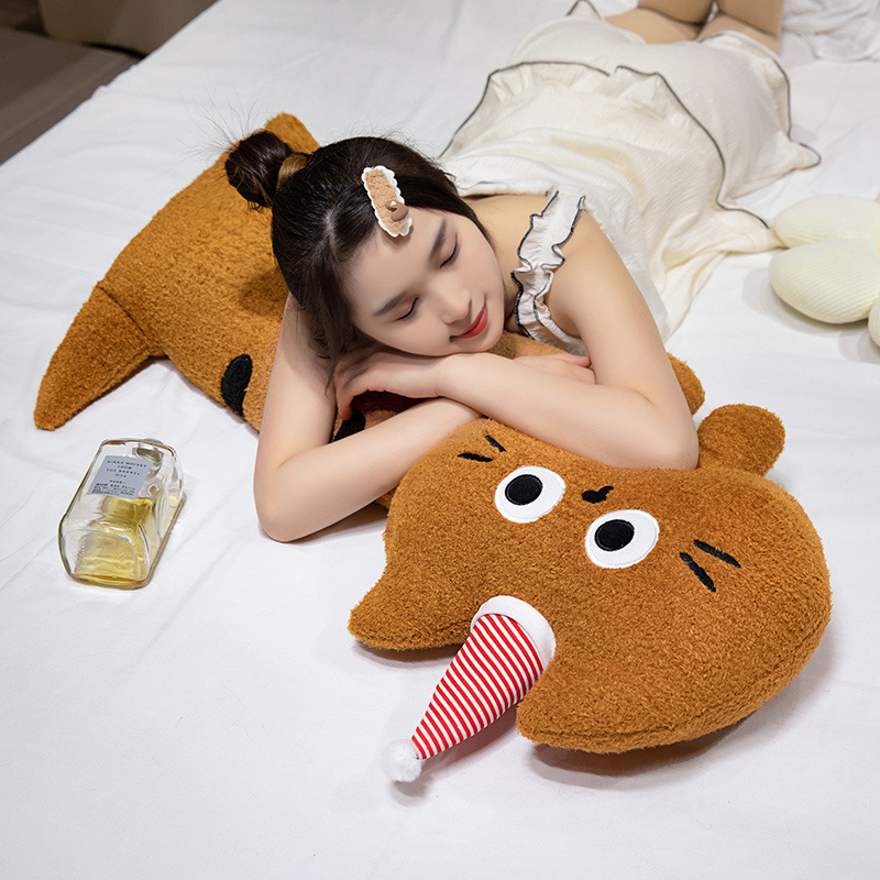 Big-eyed cat plush pillow in brown, soft long body cushion used for hugging and resting, cozy bedroom setting for relaxation and naps