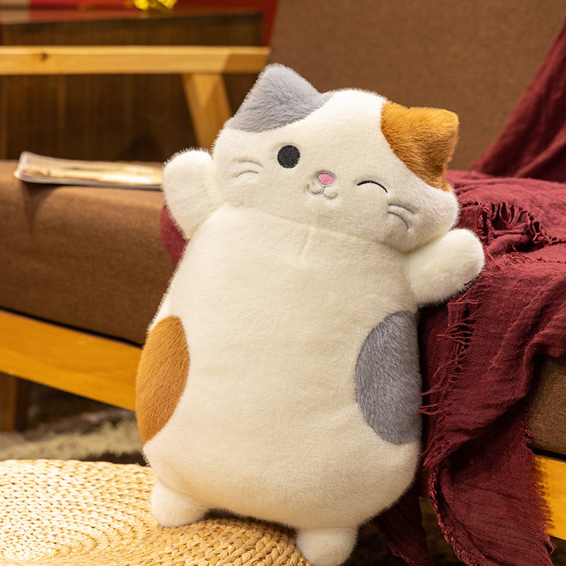 Calico cat plush pillow standing on stool beside sofa, soft fluffy texture with cute embroidered face, cozy home decor accent for living room