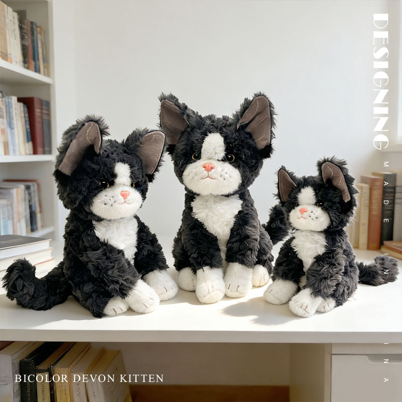 Bicolor Devon Rex cat plush toy with big ears and fluffy texture, displayed on a desk shelf in a cozy home setting