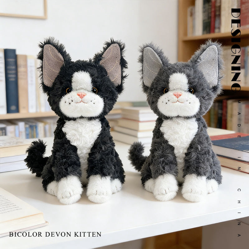 Bicolor Devon Rex cat plush toy with oversized ears and soft fluffy texture, displayed on a desk in a cozy home setting