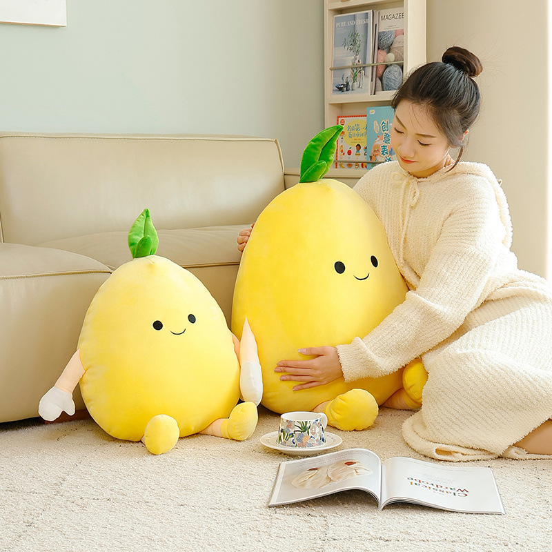 Pomelo plush pillow in two sizes with soft yellow fabric and cute face, placed on the floor beside a sofa for cozy lounging and decorative home styling
