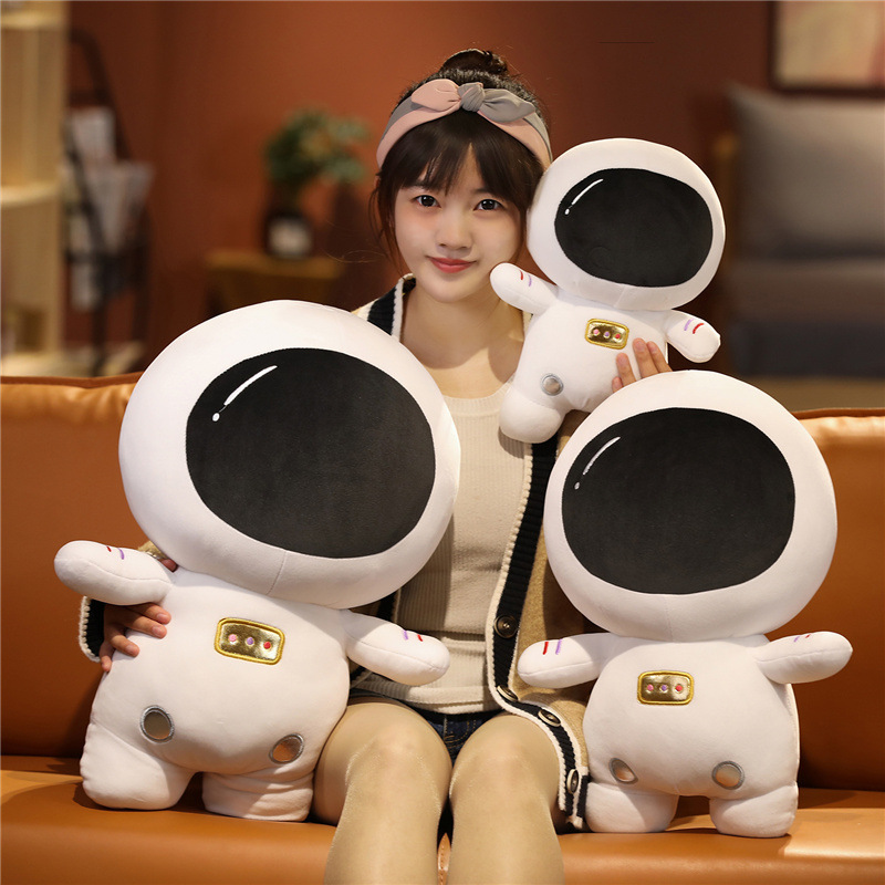 Astronaut plush toy in multiple sizes displayed on a sofa, featuring a soft white spacesuit design and cozy space-themed decor style