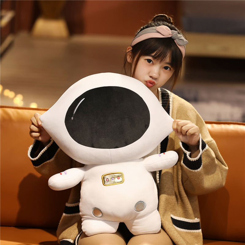 Soft astronaut plush toy featuring a large black visor and plush white spacesuit design in a warm indoor setting