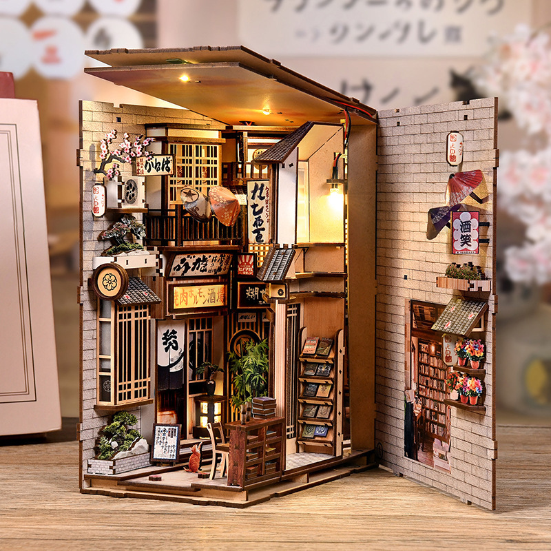 Open-view DIY book nook showing detailed Japanese alley interiors, warm lighting effects, miniature storefronts, wooden textures, and layered street scenery