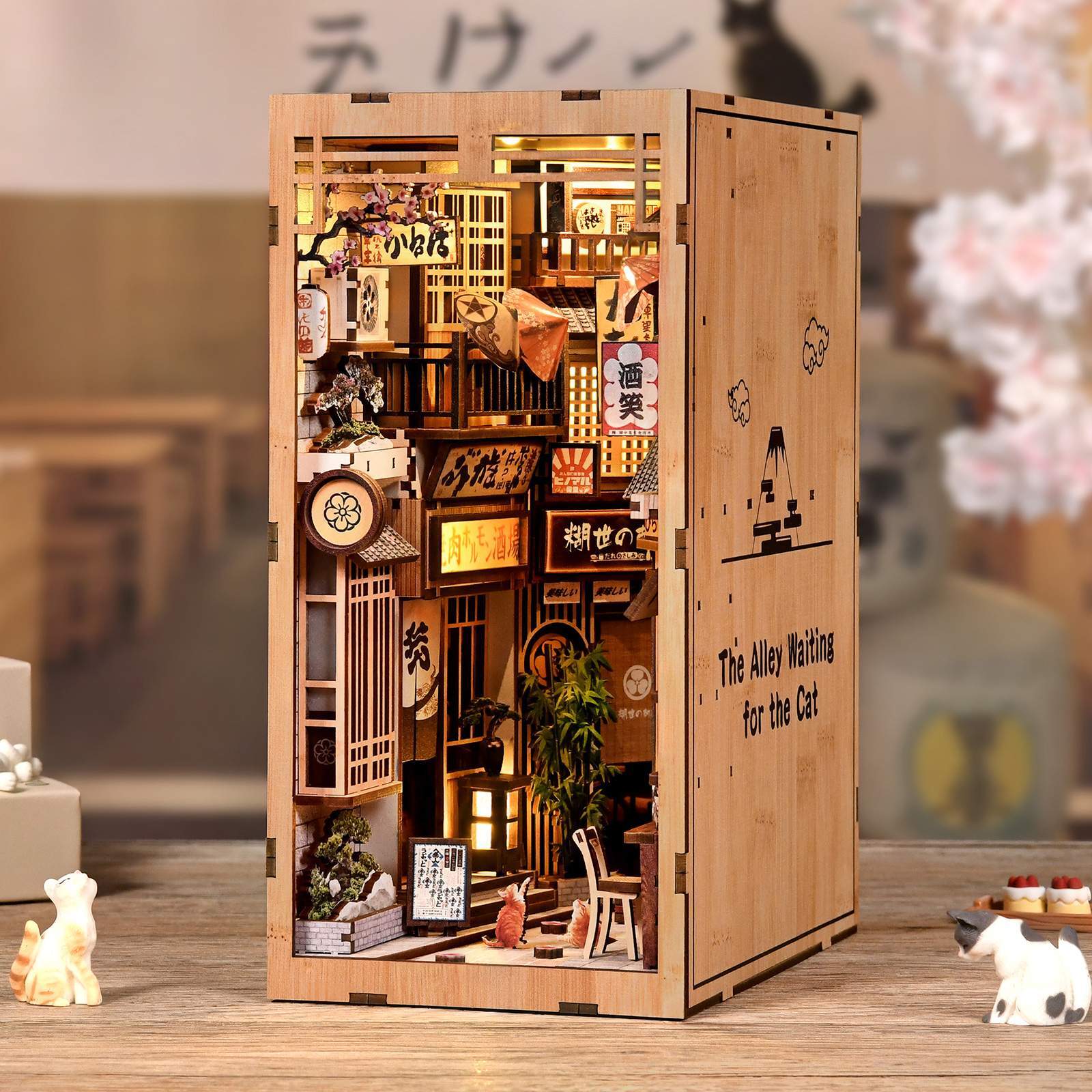Warmly lit Japanese alley style DIY book nook with detailed wooden storefronts, hanging signs, miniature decor, and cozy bookshelf display design