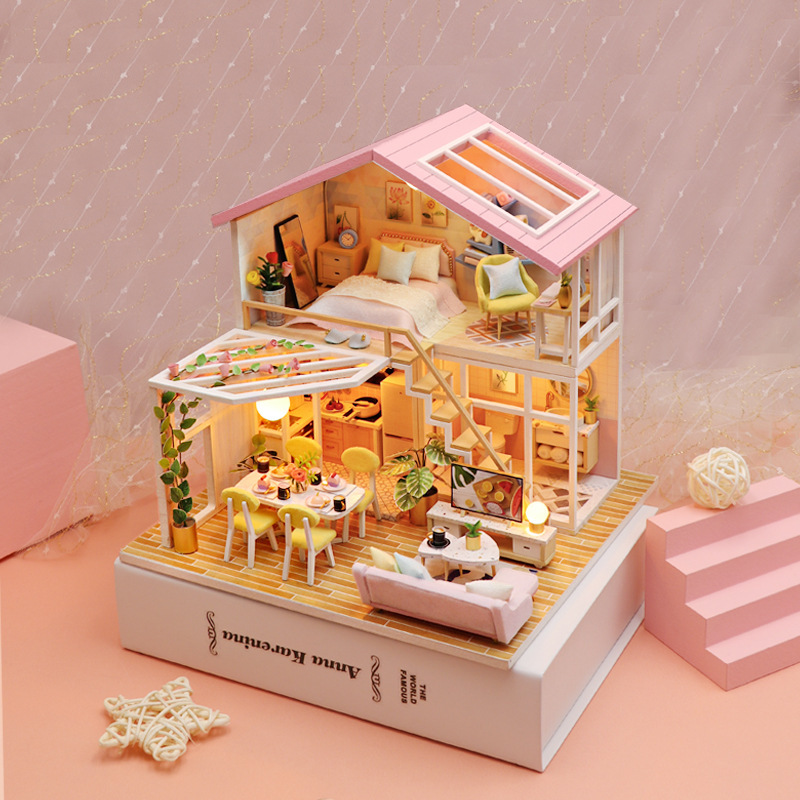 Pastel-themed DIY miniature house with warm LED lighting, detailed bedroom and dining areas, and cozy handcrafted decor displayed on a decorative book stand