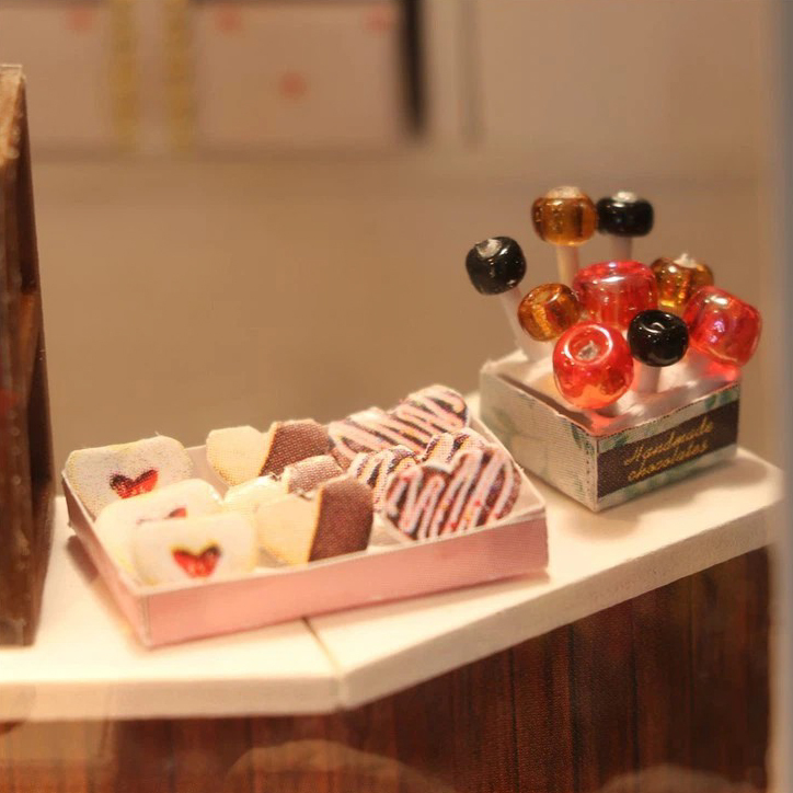 Detailed DIY miniature sweets display featuring chocolate treats, colorful candy sticks, and warm bakery-style shop atmosphere with realistic handmade accessories