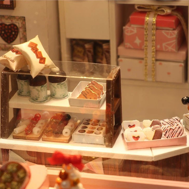 Close-up of miniature dessert counter with handmade chocolates, pastries, candy displays, and gift boxes inside a cozy DIY chocolate shop scene