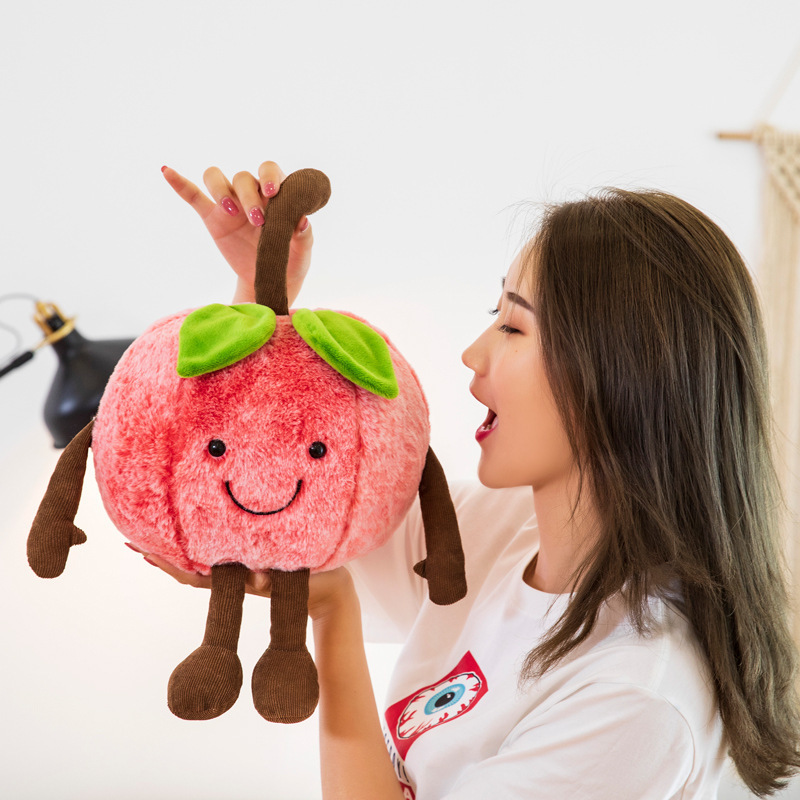 Smiling cherry plush toy with soft plush fabric, embroidered facial details, and dangling arms and legs, showcasing the playful fruit-inspired design and cuddly character
