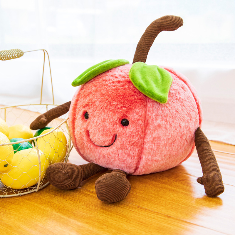 Smiling cherry plush toy with soft plush fabric, embroidered facial details, and dangling arms and legs, displayed beside decorative fruit for a cozy and cheerful home setting