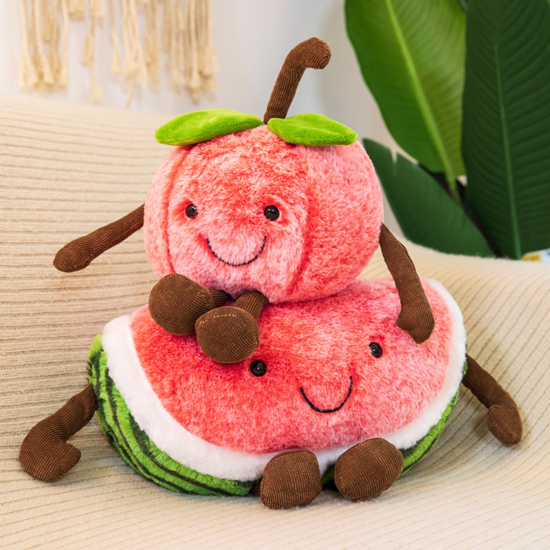 Smiling cherry and watermelon plush toys stacked together on a sofa, featuring soft plush fabric, embroidered faces, and playful dangling arms and legs
