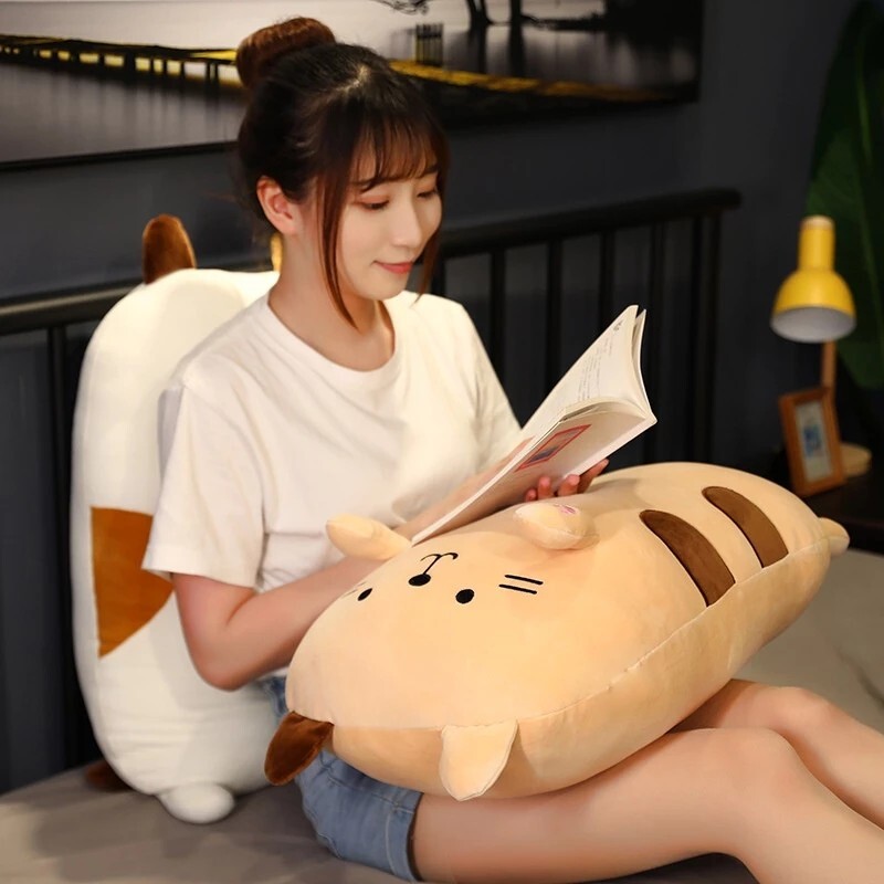 Brown Cat Plush Pillow used as a soft lap cushion while reading in a cozy bedroom setting