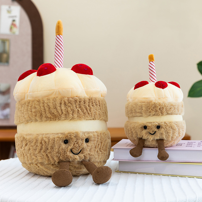 Birthday Cake Plush Toys in two sizes displayed on books, featuring soft plush textures, smiling faces, and dangling legs for playful room decor