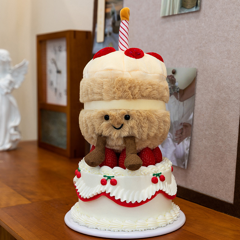 Birthday Cake Plush Toy displayed on a decorative cake stand, featuring a smiling face, soft cake-inspired layers, plush candle detail, and dangling legs