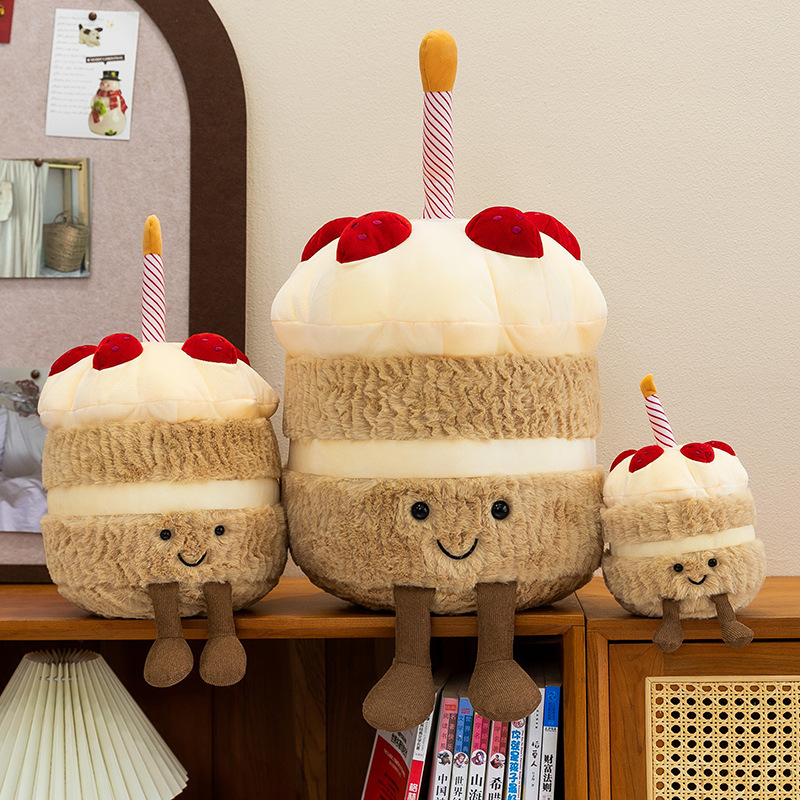 Birthday Cake Plush Toys in 15 cm, 25 cm, and 35 cm sizes displayed on a wooden shelf, featuring smiling faces, soft cake-inspired layers, and dangling legs