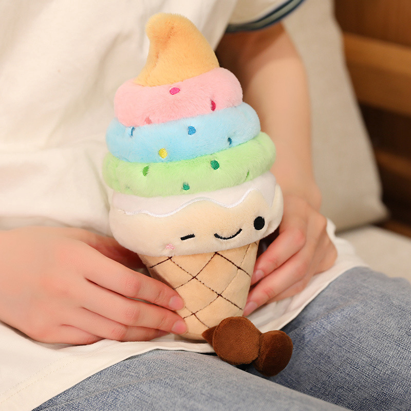 Rainbow Ice Cream Plush Toy featuring colorful soft serve layers, embroidered winking face, and dangling legs, resting comfortably on a lap