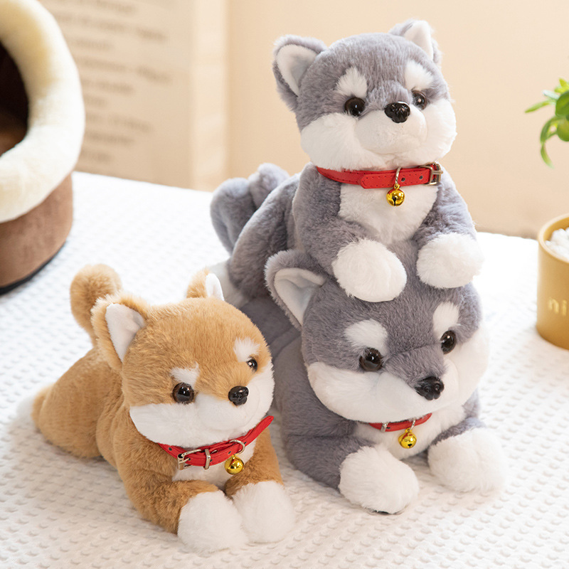 Shiba Inu plush toys in brown and gray displayed together on a bed, showcasing different sizes and color options