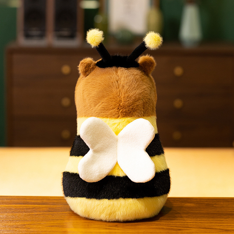 Back view of Bee Capybara Plush Toy featuring fluffy white wings, fuzzy antennae, and bee-inspired striped details in a cozy indoor setting