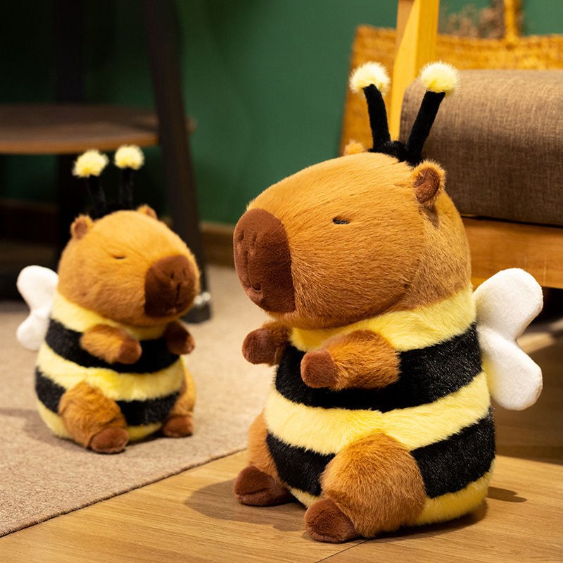 Bee Capybara Plush Toy displayed on a wooden floor in a cozy room setting, showcasing soft plush texture, bee-inspired stripes, fluffy wings, and whimsical animal decor charm