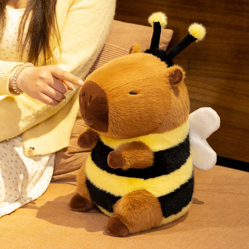 Bee Capybara Plush Toy displayed on a bed, highlighting its cuddly size, soft plush texture, fluffy wings, and bee-inspired striped design