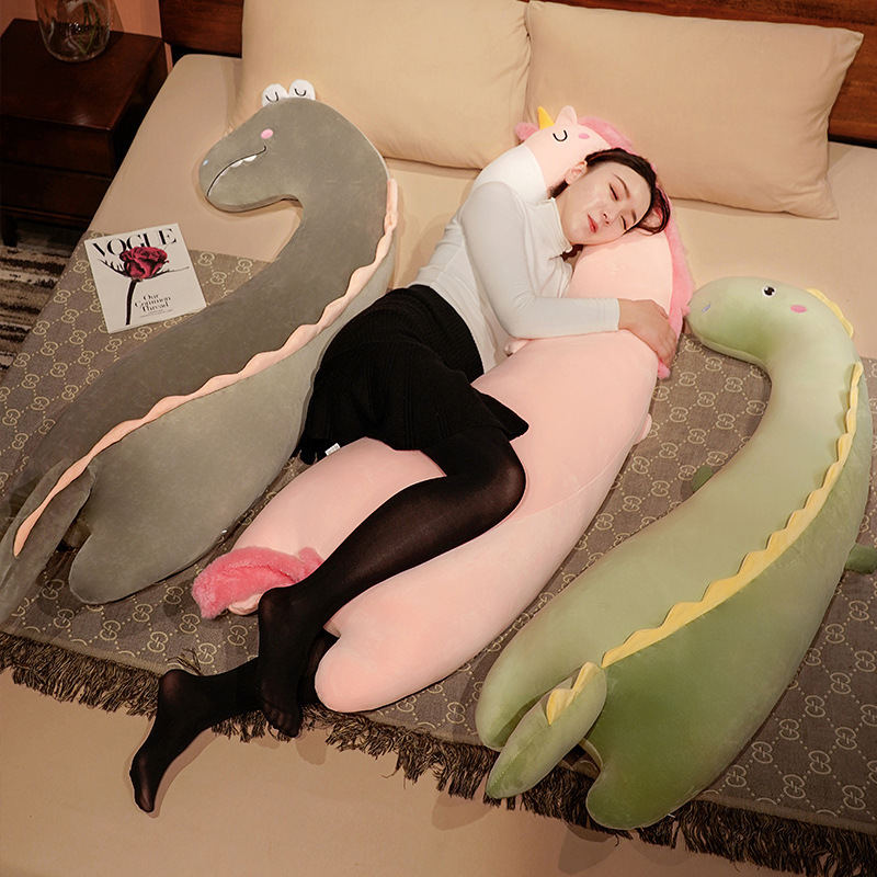 Unicorn, Sleepy Eyes Dinosaur, and Round Eyes Dinosaur long plush pillows displayed as sleeping and leg-hugging body pillows on a bed