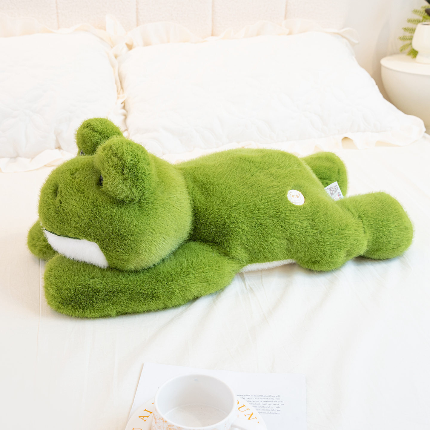 Cute Frog Plush Toy resting on a bed, featuring a cozy lying frog design for relaxing, cuddling, and bedroom decor