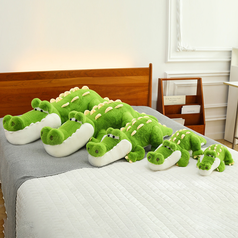 Cute Crocodile Plush Pillow in multiple sizes displayed on a bed, featuring a long crocodile body, soft plush fabric, and cheerful green design