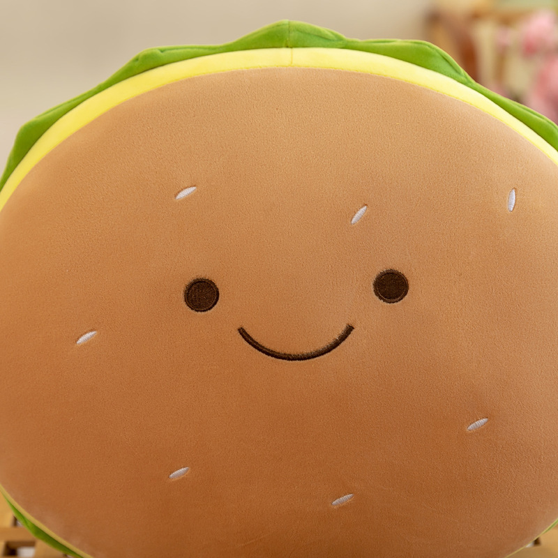 Close-up of the cute burger plush pillow featuring an embroidered smiling face, soft plush fabric, and adorable food-inspired design with stitched sesame seed details