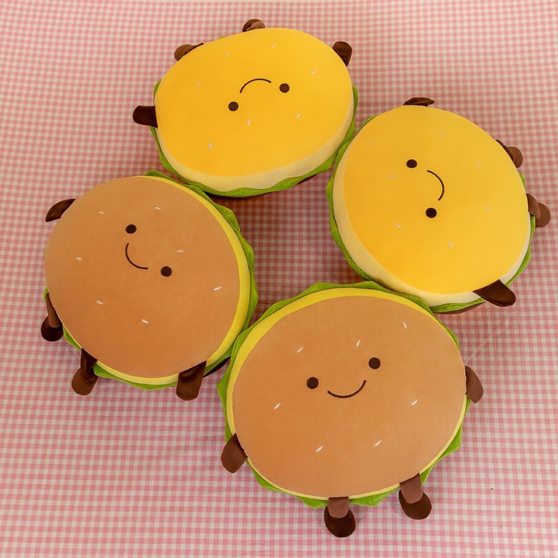 Cute burger plush pillows in yellow and brown color options displayed from a top view, featuring smiling faces, soft plush fabric, and playful food-inspired home decor