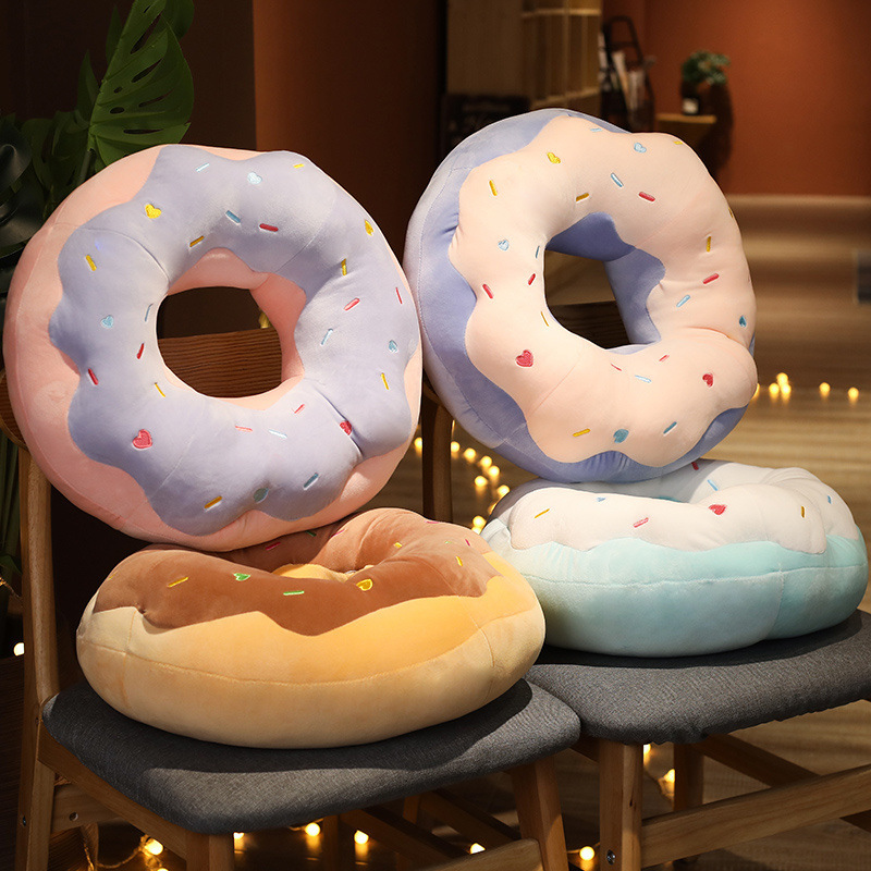 Donut Plush Pillows in raspberry, taro, sea salt, and chocolate designs displayed on chairs