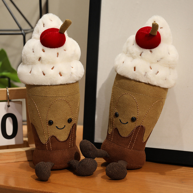 Cute chocolate milkshake plush toys with soft plush fabric, embroidered smiling faces, whipped cream topping, and cherry detail on a tabletop display