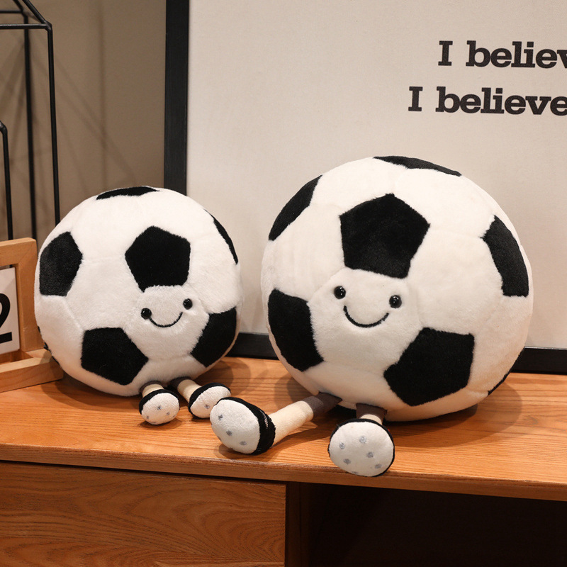 Soccer Ball Plush Toys in two sizes with smiling faces and dangling legs displayed together on a wooden tabletop