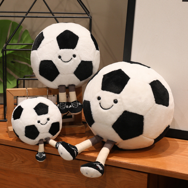Soccer Ball Plush Toys in multiple sizes with smiling faces and dangling legs displayed on a wooden tabletop