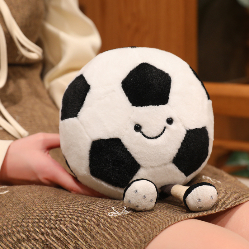Soccer Ball Plush Toy with a smiling face and dangling legs resting comfortably, showcasing its soft plush fabric and cuddly design