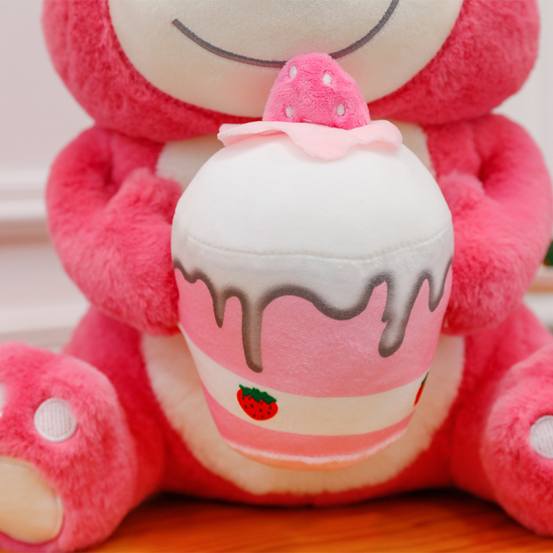 Close-up of the strawberry cake accessory on the Pink Bear Plush Toy, showcasing soft plush fabric, embroidered icing details, and a cute strawberry design