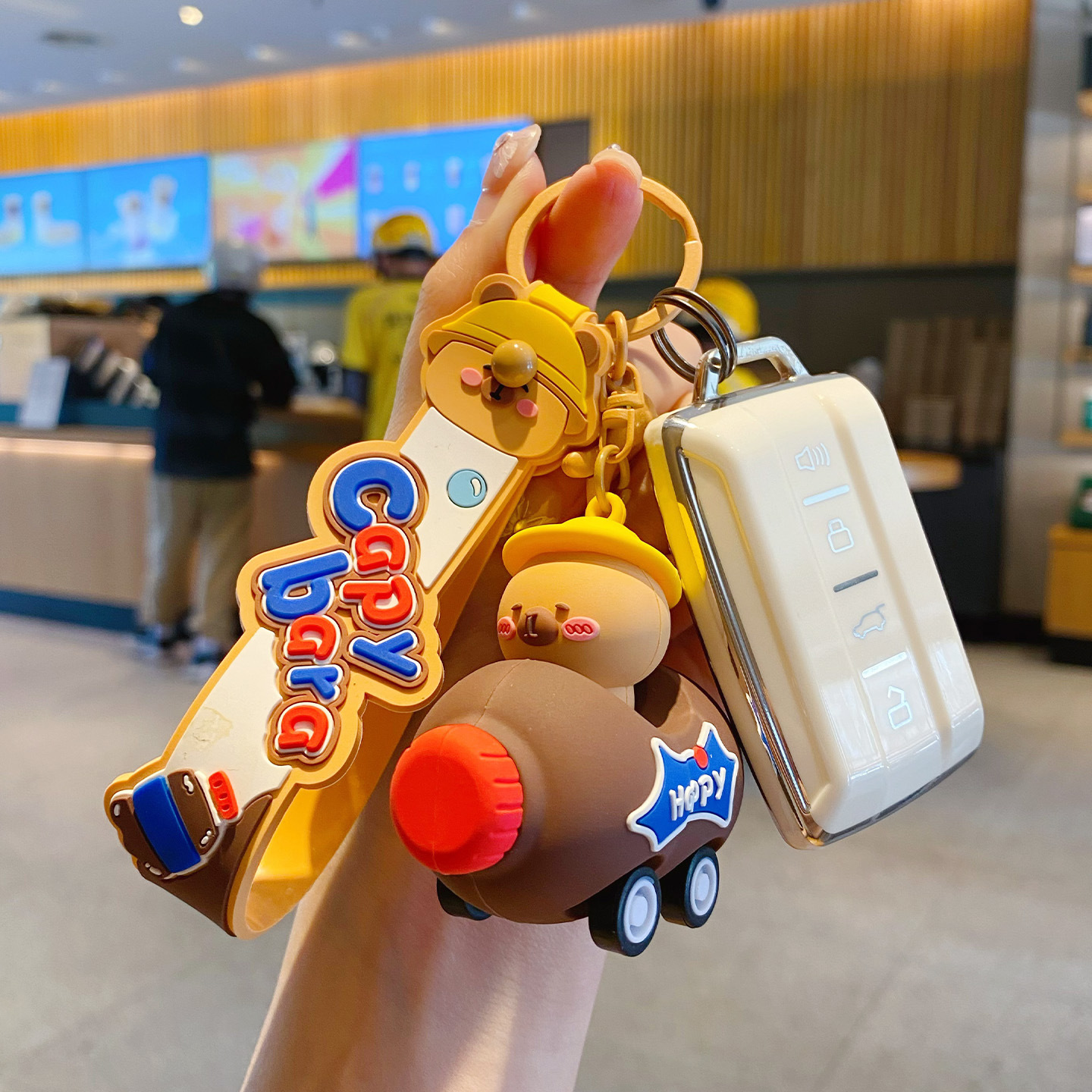 Cute capybara in a brown cola bottle car keychain charm attached to a car key fob